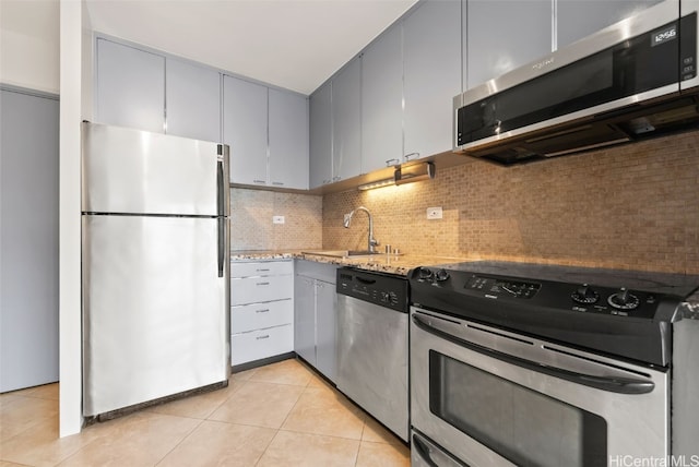 kitchen with sink, light tile patterned floors, appliances with stainless steel finishes, tasteful backsplash, and light stone counters