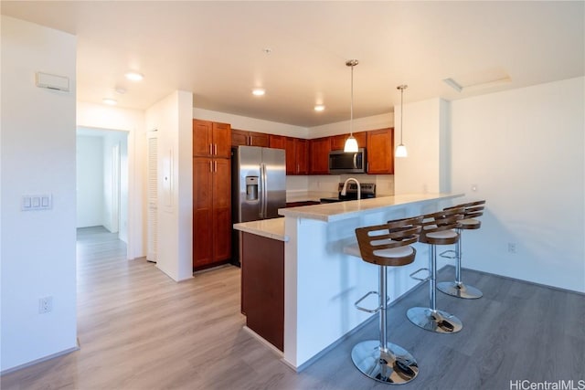 kitchen with decorative light fixtures, stainless steel appliances, light countertops, a peninsula, and a kitchen breakfast bar