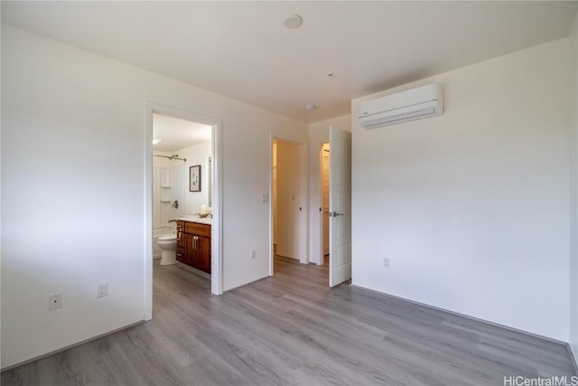 unfurnished bedroom featuring an AC wall unit, connected bathroom, and light wood-style flooring