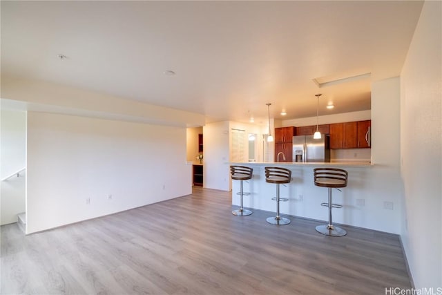 kitchen with a peninsula, light wood-type flooring, stainless steel refrigerator with ice dispenser, and a kitchen breakfast bar