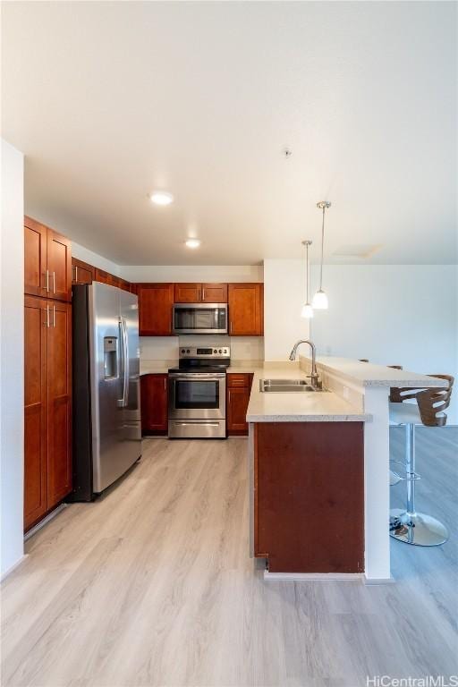 kitchen featuring appliances with stainless steel finishes, pendant lighting, sink, a kitchen bar, and light hardwood / wood-style flooring