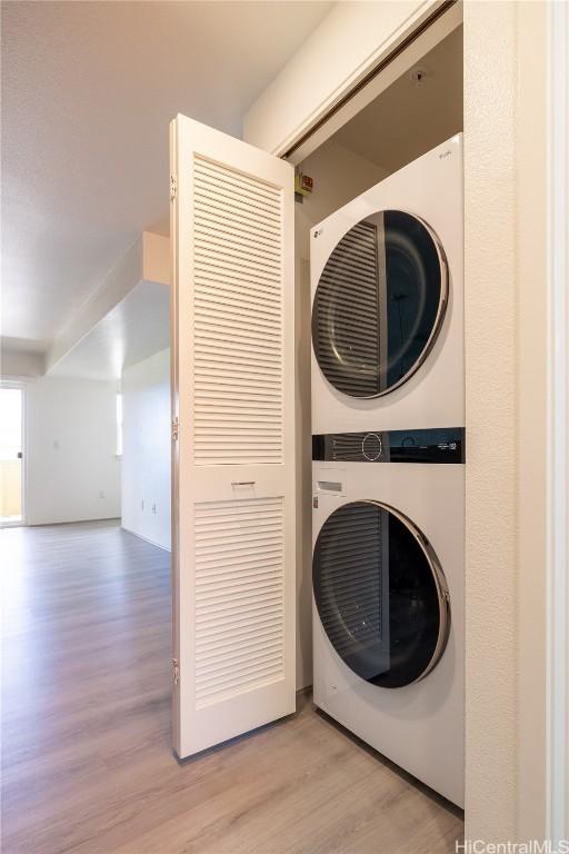 laundry room with stacked washer / drying machine, laundry area, and light wood finished floors