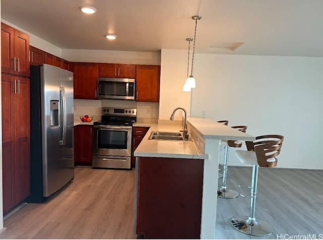 kitchen featuring a kitchen bar, sink, appliances with stainless steel finishes, kitchen peninsula, and pendant lighting