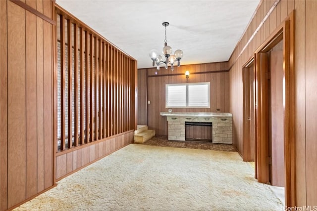 interior space featuring a stone fireplace, wooden walls, a notable chandelier, pendant lighting, and carpet