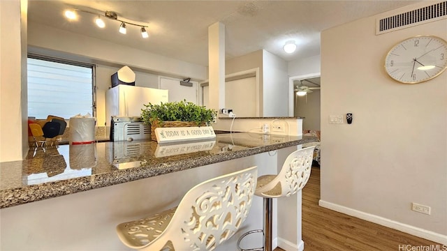 kitchen featuring a breakfast bar area, dark hardwood / wood-style flooring, dark stone counters, ceiling fan, and kitchen peninsula