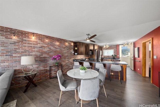 dining space featuring dark hardwood / wood-style flooring, ceiling fan with notable chandelier, and brick wall