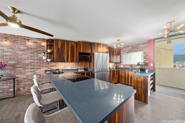 kitchen featuring black appliances, a breakfast bar area, kitchen peninsula, an inviting chandelier, and light hardwood / wood-style flooring