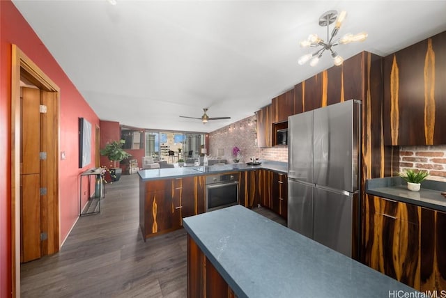 kitchen with decorative backsplash, hanging light fixtures, kitchen peninsula, stainless steel appliances, and dark wood-type flooring