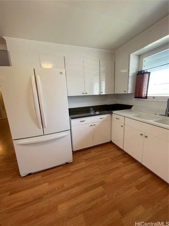 kitchen with sink, white cabinetry, light hardwood / wood-style flooring, white refrigerator, and ornamental molding