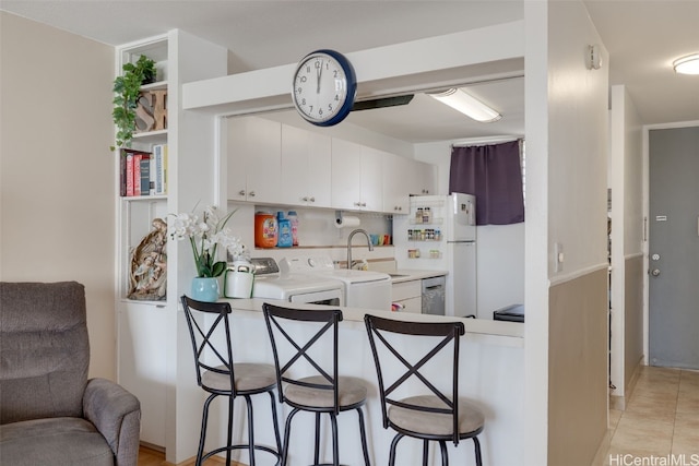 kitchen with sink, a breakfast bar area, washer / clothes dryer, and white cabinets