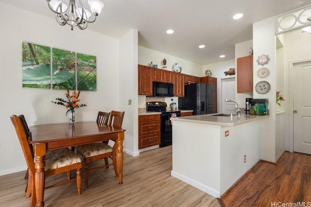 kitchen featuring black appliances, sink, hanging light fixtures, kitchen peninsula, and light hardwood / wood-style flooring