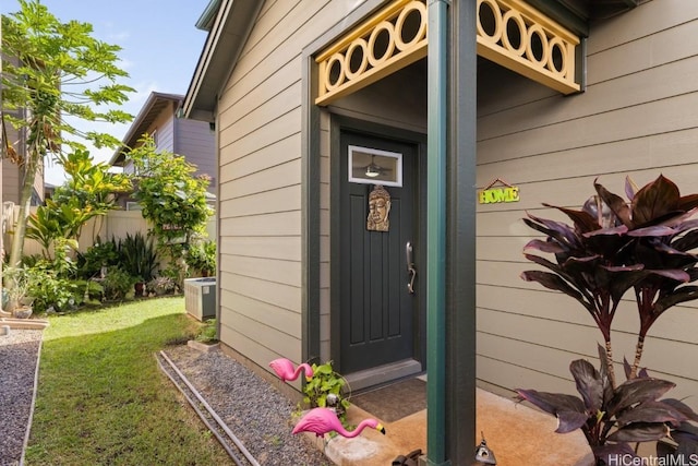 view of exterior entry featuring central AC unit and a lawn