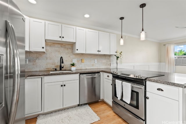 kitchen with a peninsula, a sink, white cabinets, appliances with stainless steel finishes, and crown molding