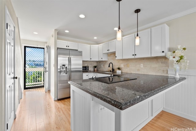 kitchen with light wood finished floors, white cabinets, appliances with stainless steel finishes, a peninsula, and a sink