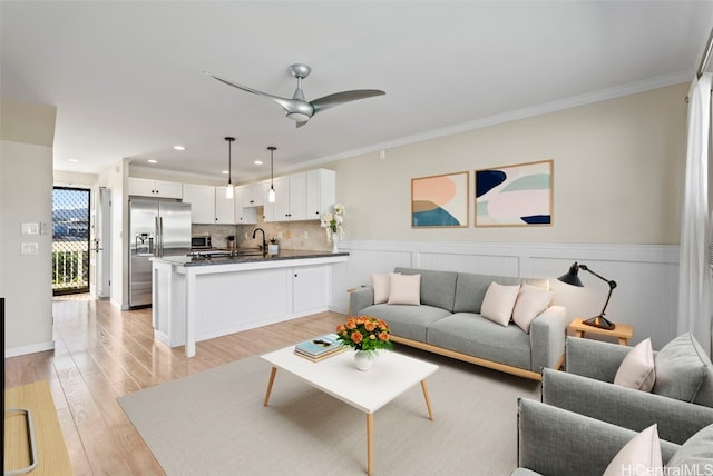 living room featuring light wood-style floors, wainscoting, crown molding, and a ceiling fan