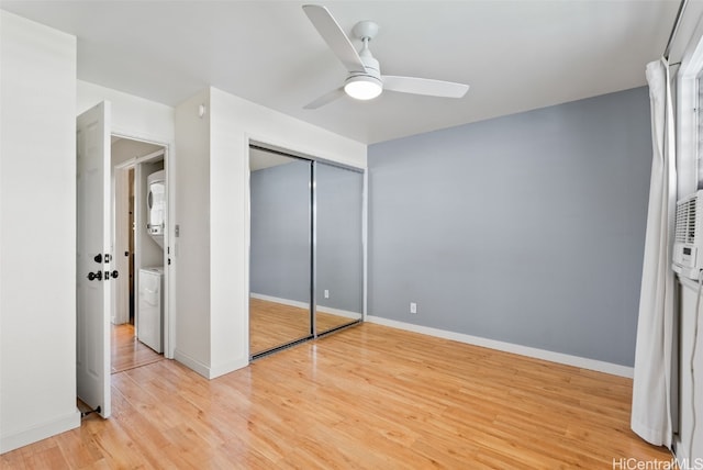 unfurnished bedroom featuring a closet, a ceiling fan, stacked washing maching and dryer, light wood-type flooring, and baseboards