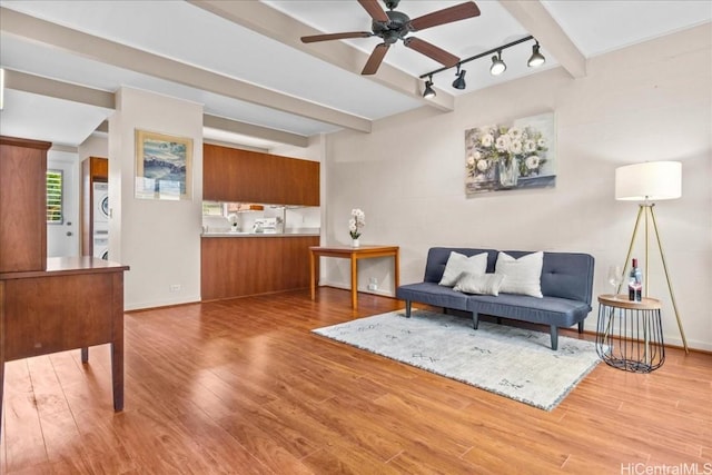 living room with rail lighting, stacked washer and dryer, beam ceiling, ceiling fan, and light wood-type flooring