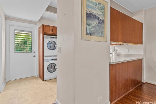 laundry area with stacked washer / dryer, light tile patterned flooring, and cabinets