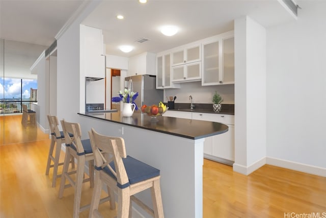 kitchen featuring kitchen peninsula, stainless steel refrigerator, white cabinets, and a kitchen bar