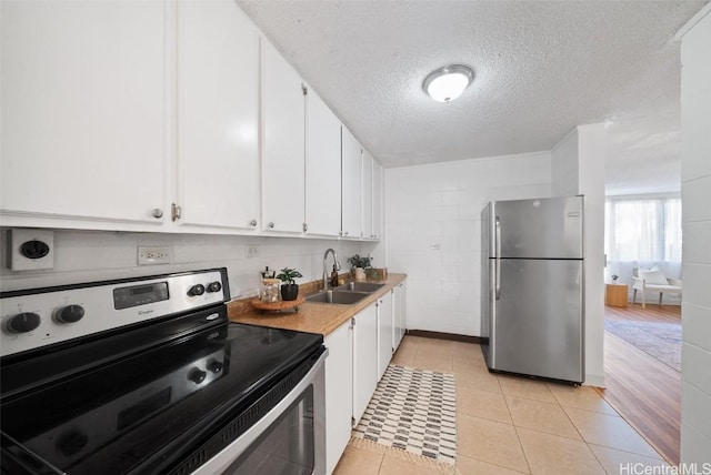 kitchen featuring light tile patterned flooring, sink, a textured ceiling, appliances with stainless steel finishes, and white cabinets