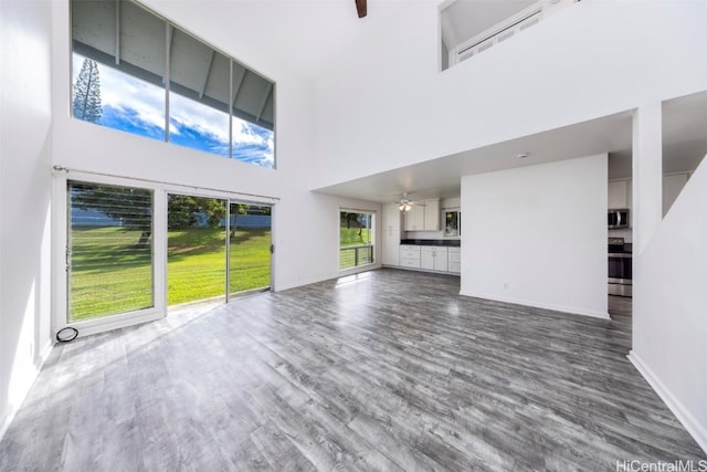 unfurnished living room with a ceiling fan, a high ceiling, baseboards, and wood finished floors