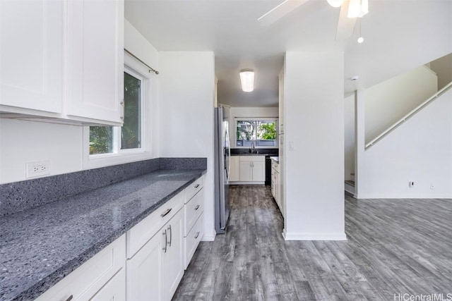 kitchen featuring freestanding refrigerator, white cabinetry, a sink, dark stone countertops, and wood finished floors