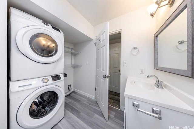 clothes washing area with stacked washer / drying machine, a sink, wood finished floors, laundry area, and baseboards