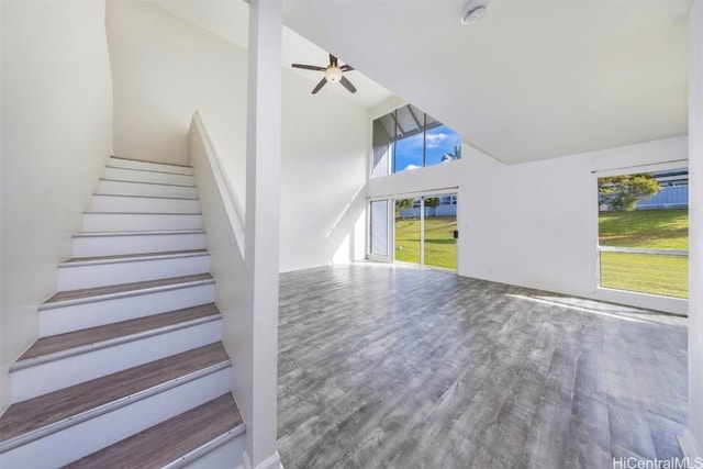 stairs with high vaulted ceiling, ceiling fan, and wood finished floors