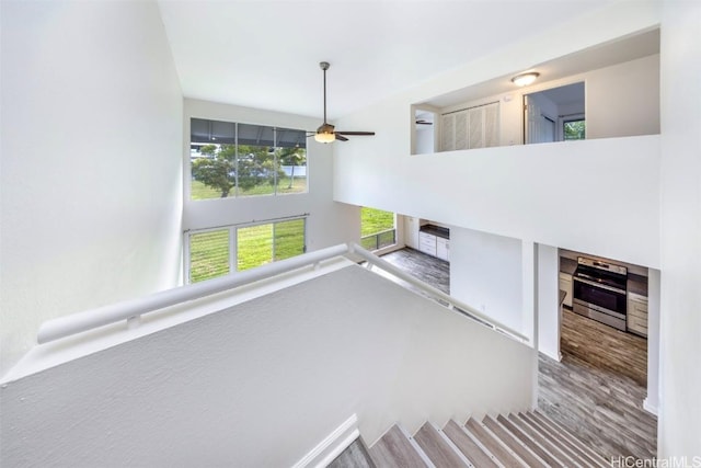 staircase featuring a towering ceiling, ceiling fan, and hardwood / wood-style flooring