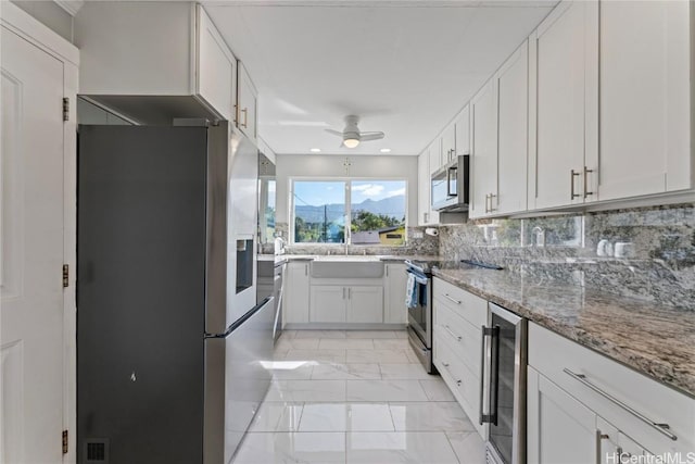 kitchen featuring sink, white cabinetry, stainless steel appliances, light stone countertops, and beverage cooler