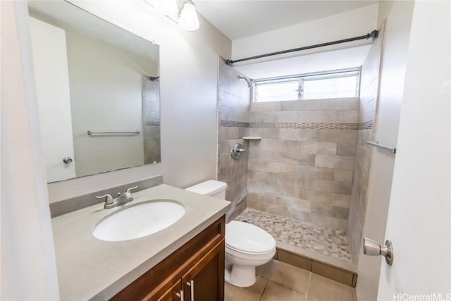 bathroom with a tile shower, vanity, tile patterned floors, and toilet