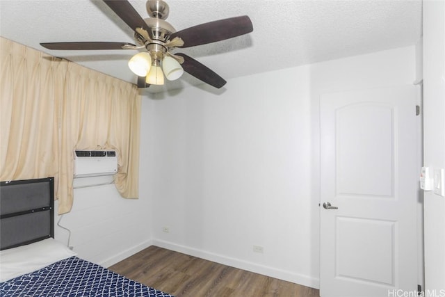 unfurnished bedroom featuring ceiling fan, dark wood-type flooring, an AC wall unit, and a textured ceiling