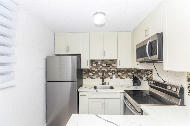 kitchen with sink, light stone countertops, white cabinets, and appliances with stainless steel finishes