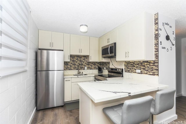 kitchen featuring sink, stainless steel appliances, dark hardwood / wood-style floors, a kitchen breakfast bar, and white cabinets