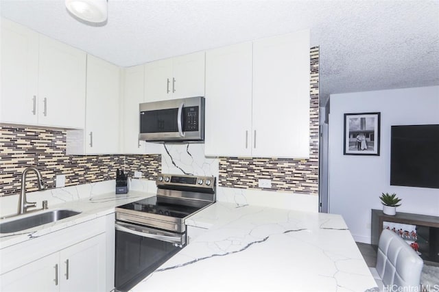 kitchen featuring sink, light stone counters, tasteful backsplash, stainless steel appliances, and white cabinets