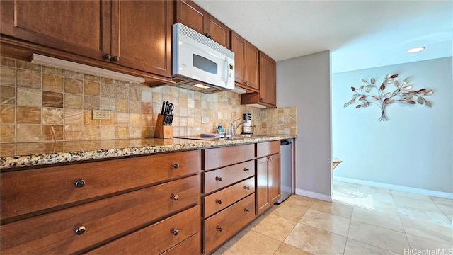 kitchen featuring tasteful backsplash, light stone countertops, stainless steel dishwasher, and light tile patterned floors