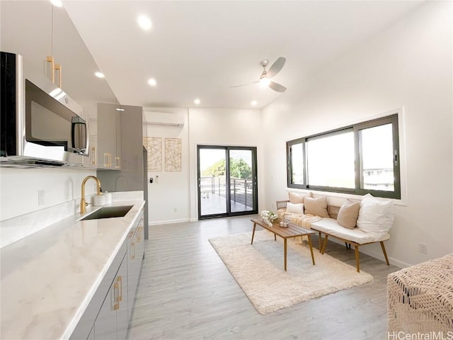 living room with sink, a wall mounted air conditioner, ceiling fan, and light hardwood / wood-style flooring