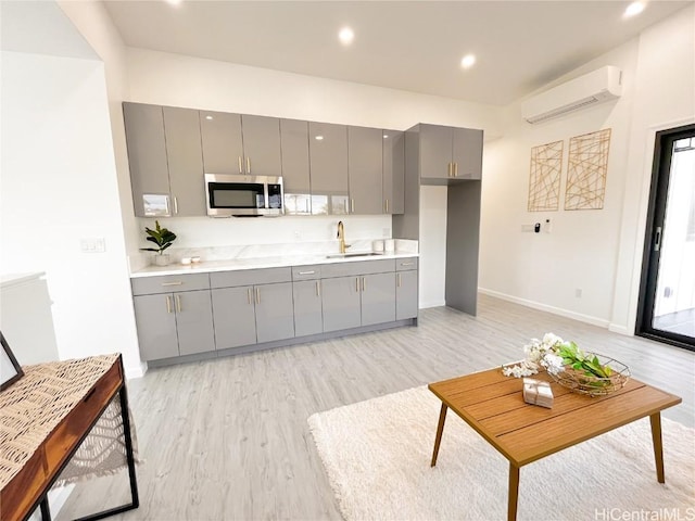 kitchen with a wall mounted AC, sink, light hardwood / wood-style flooring, and gray cabinetry