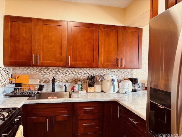 kitchen featuring gas stove, sink, light stone counters, stainless steel fridge, and backsplash