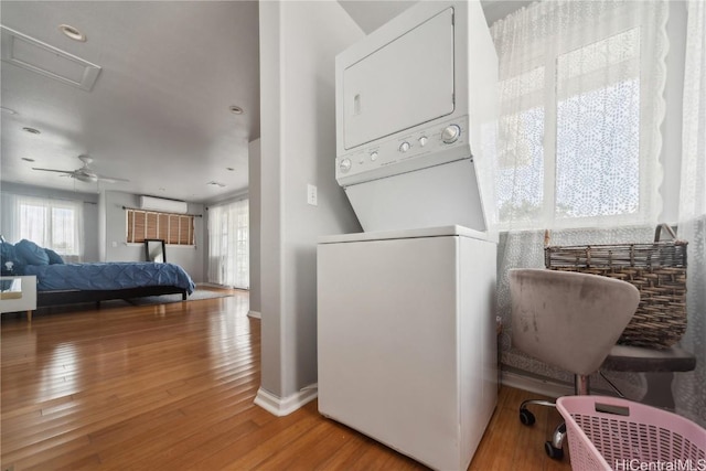 clothes washing area with stacked washer / drying machine, a wall mounted air conditioner, hardwood / wood-style floors, and ceiling fan