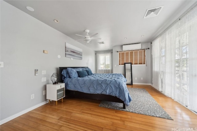 bedroom with ceiling fan, an AC wall unit, and light wood-type flooring