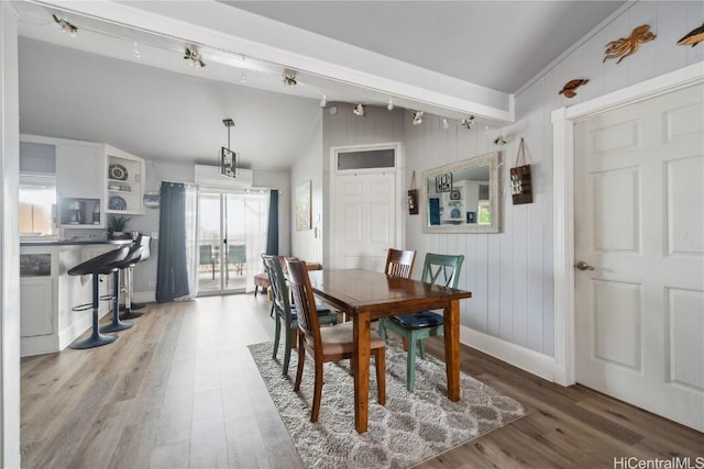 dining space with vaulted ceiling, wood walls, and light hardwood / wood-style flooring