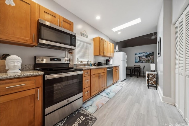 kitchen with sink, light stone counters, light hardwood / wood-style flooring, appliances with stainless steel finishes, and vaulted ceiling with skylight