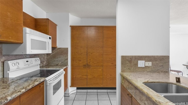 kitchen featuring sink, light tile patterned floors, white appliances, light stone counters, and decorative backsplash