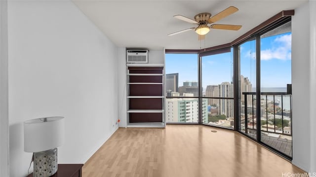 unfurnished room featuring ceiling fan, a wall of windows, light hardwood / wood-style floors, and a wall unit AC