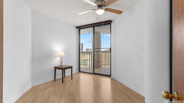 empty room featuring expansive windows, ceiling fan, and light wood-type flooring