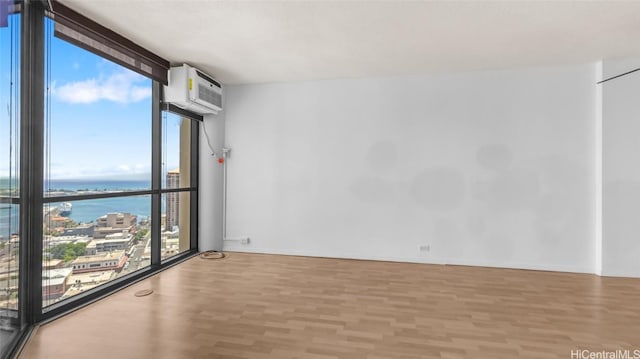 spare room with a wall of windows, light hardwood / wood-style floors, a wall unit AC, and a water view