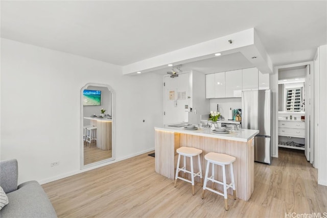 kitchen with stainless steel fridge, a kitchen bar, light hardwood / wood-style floors, white cabinets, and a center island with sink