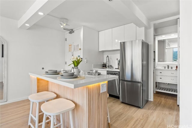 kitchen with sink, appliances with stainless steel finishes, white cabinetry, a center island, and a kitchen bar