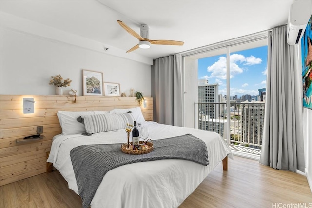 bedroom featuring light hardwood / wood-style flooring, ceiling fan, floor to ceiling windows, access to outside, and an AC wall unit